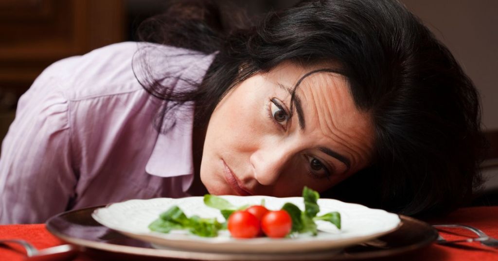 Image of a woman looking desperately at a plate of cherry tomatoes